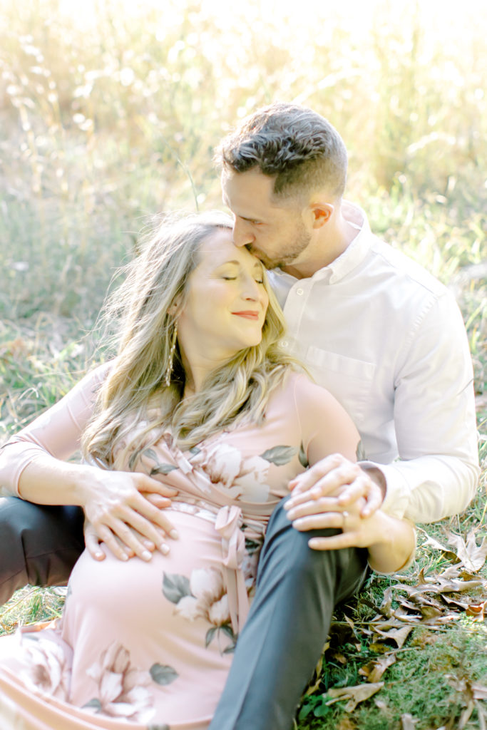 athens georiga maternity session photo of couple sitting in field kissing