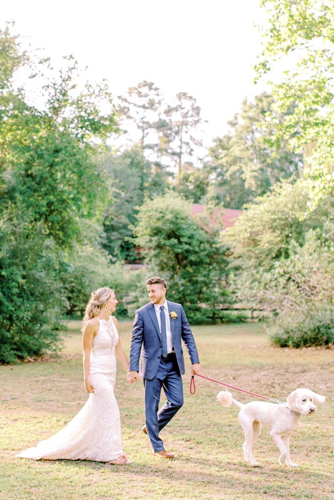 bride and groom walk and laugh with their golden doodle dog, holding hands | photo by mary catherine echols