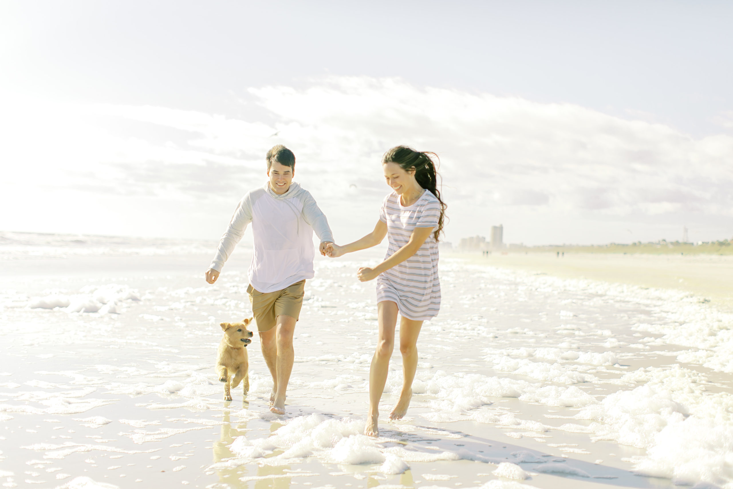 couple runs with their golden retriever puppy on atlantic beach