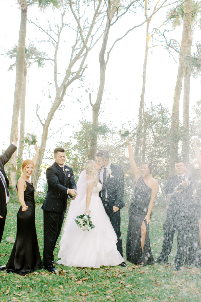 bride and groom kiss with bridal party spraying champagne at the ribault club | photo by Mary Catherine Echols, a Jacksonville based wedding photographer
